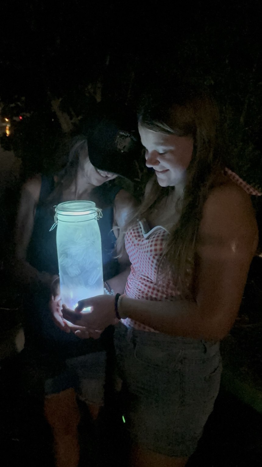 Two family members at night holding a jar glowing with bright blue light during their bioluminescence adventure