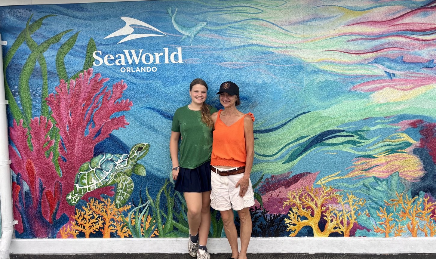 Julie and Lynley smiling together in front of a colorful SeaWorld Orlando marine-life mural